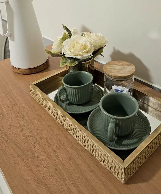 Cantinho do café da recepção da clínica: bandeja com duas xícaras verdes, garrafa térmica e um arranjo de rosas brancas