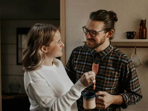 Casal rindo junto na cozinha de casa, na hora do café da manhã