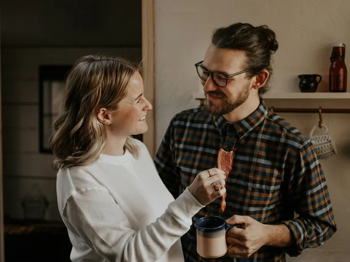Casal rindo junto na cozinha de casa, na hora do café da manhã